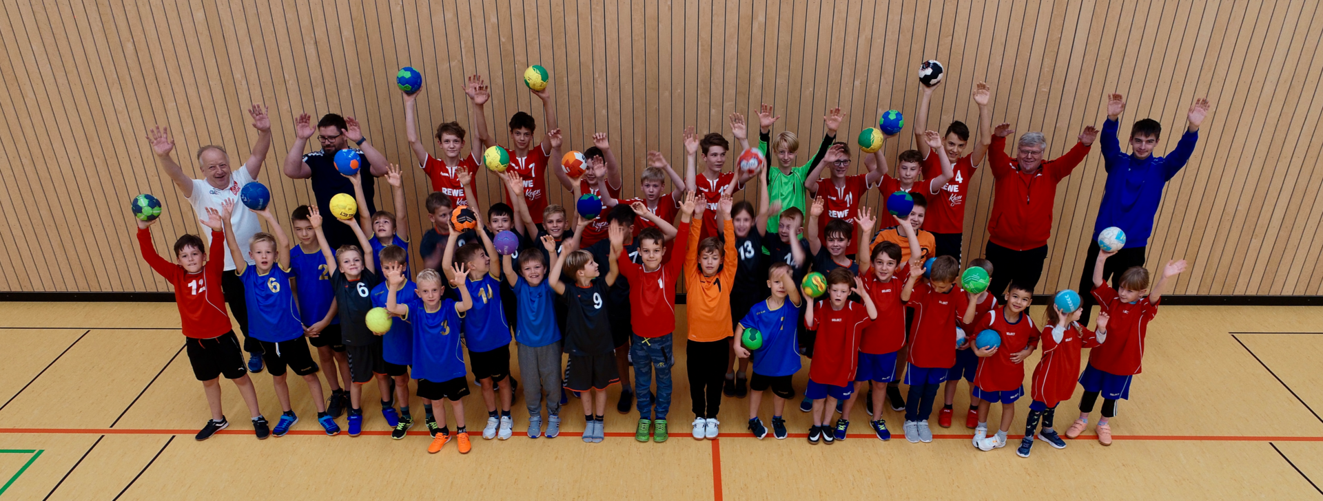Großes Jugendhandballteam der HSG Coswig mit Trainern in einer Sporthalle, viele halten Bälle hoch und jubeln.