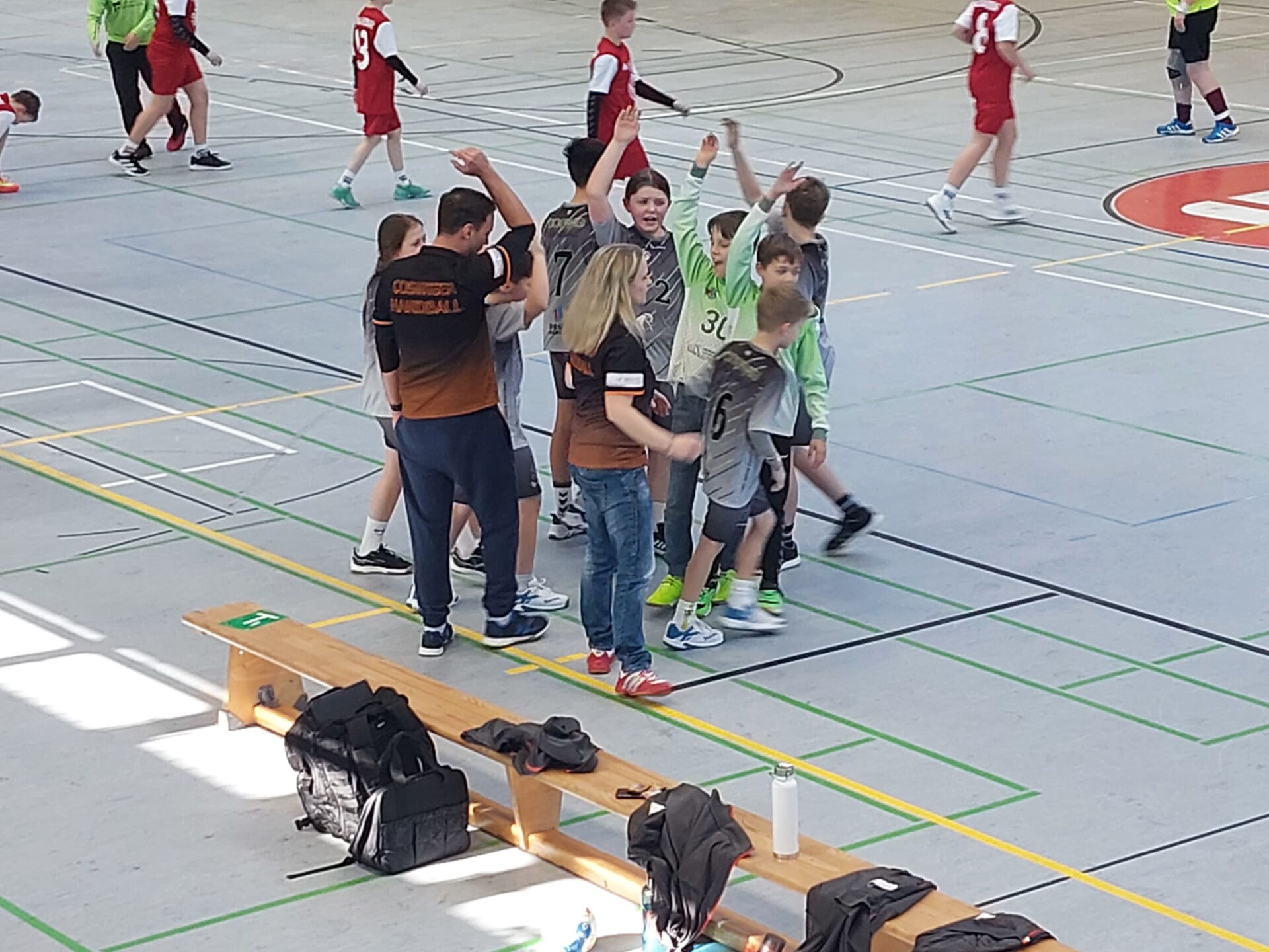 Eine Gruppe junger Handballspieler der HSG Coswig jubelt mit erhobenen Armen, umringt von Trainern, in einer Sporthalle.
