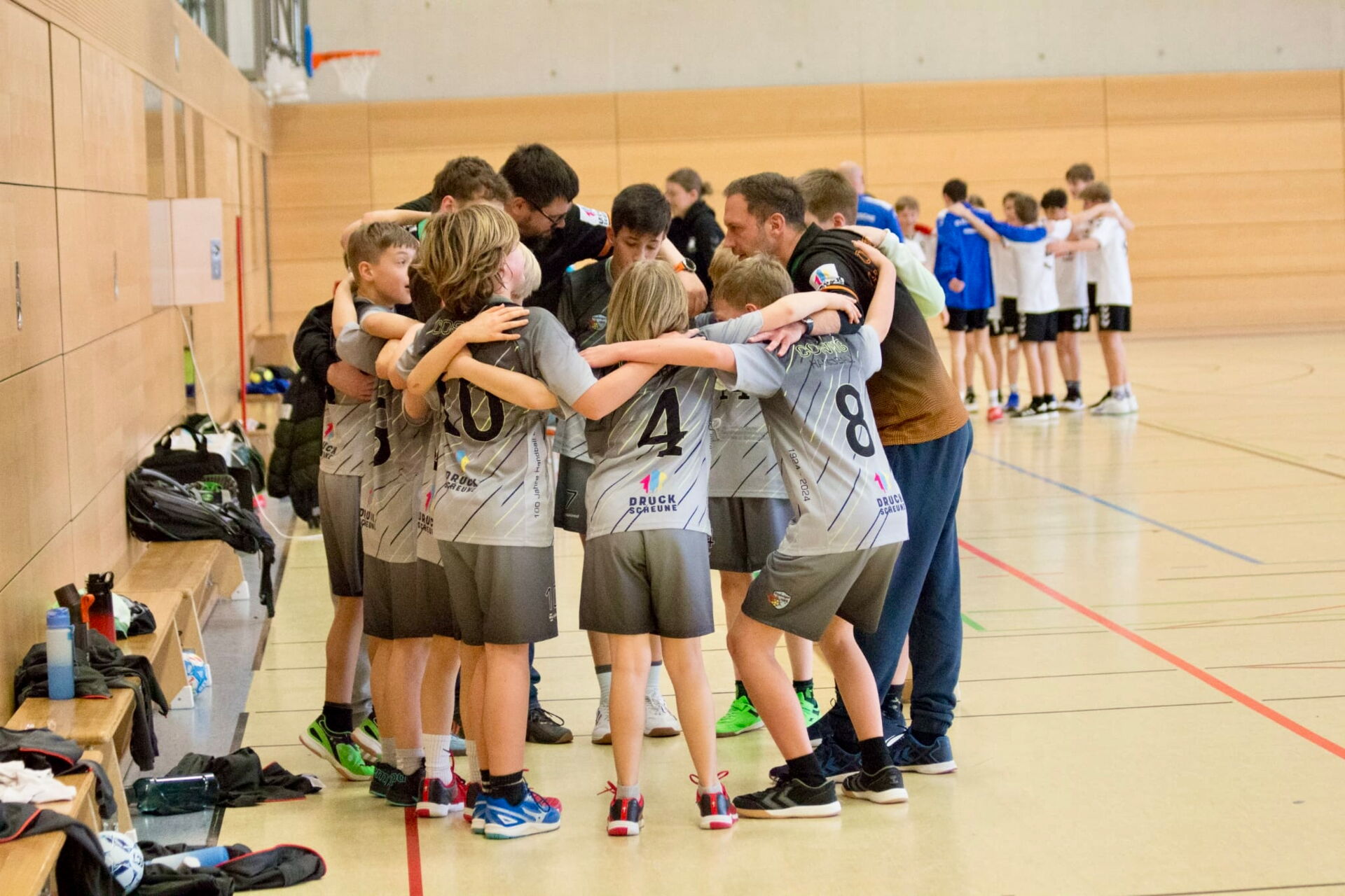 Jugendhandballteam der HSG Coswig bildet einen Huddle mit Trainern in einer Sporthalle, Arme umeinander gelegt.