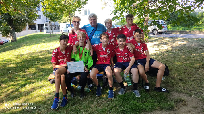 Eine Jugendhandballmannschaft der HSG Coswig mit Trainern posiert stolz mit einer Urkunde und Medaillen im Freien.