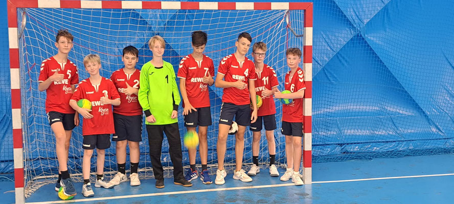 Jugendhandballteam der HSG Coswig mit Torwart vor einem Handballtor in einer Sporthalle. Alle tragen rote Trikots außer dem Torwart.