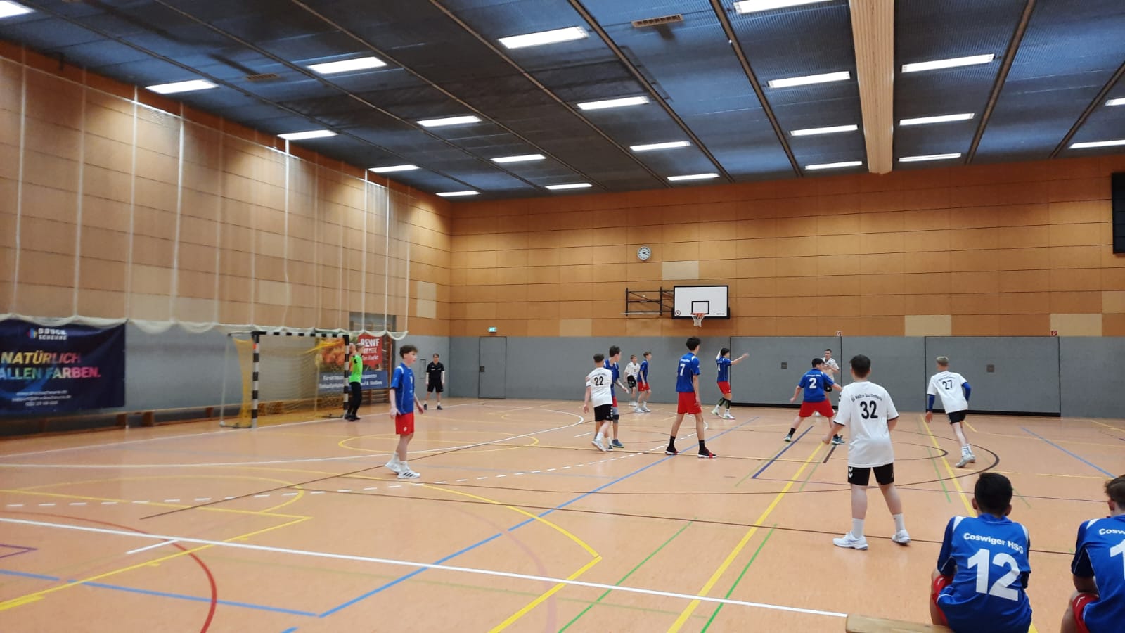 Handballspiel der HSG Coswig in einer Sporthalle mit Spielern in weißen und blauen Trikots auf dem Spielfeld.
