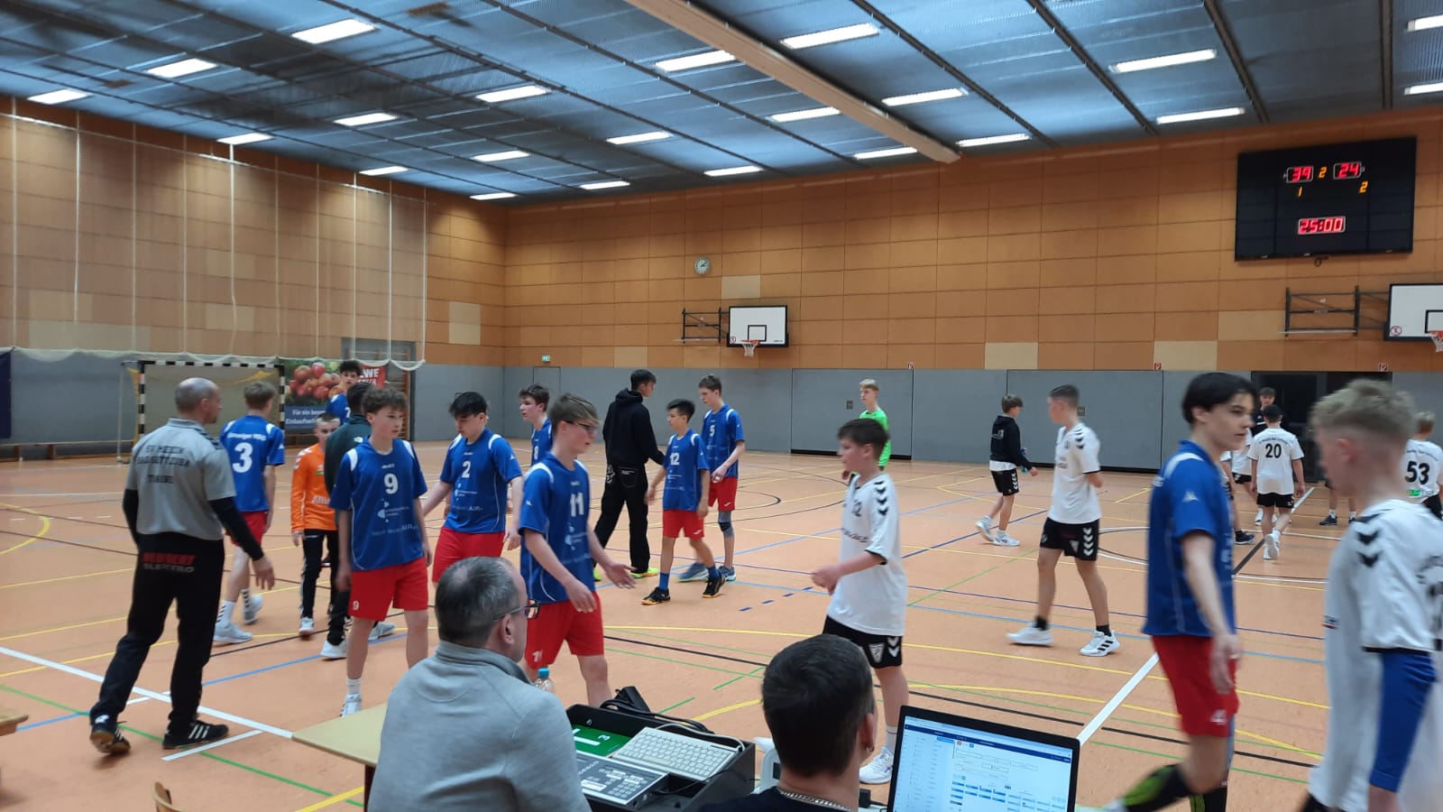Jugendhandballspiel der HSG Coswig in einer Halle. Spieler in blauen und weißen Trikots stehen auf dem Feld, Trainer besprechen Taktik.