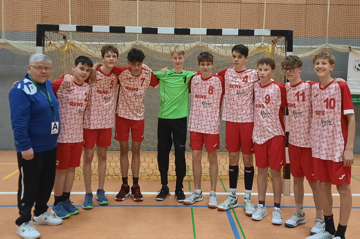 Teamfoto C-Jugend in rot/weiß gestreiften Trikots mit roter Hose vor einem Handballtor