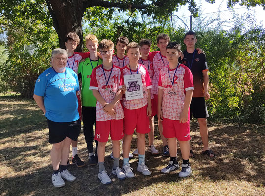 Jugendhandballteam der HSG Coswig mit Trainer posiert stolz mit einer Urkunde im Freien unter einem Baum.