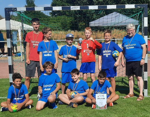 Jugendhandballteam der HSG Coswig mit Trainern posiert stolz mit Medaillen und einer Urkunde vor einem Handballtor im Freien.