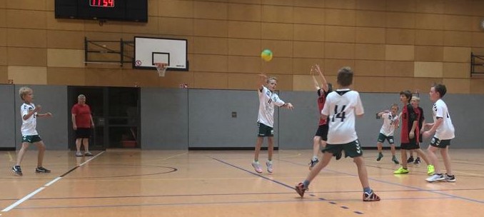 Jugendhandballspiel der HSG Coswig in einer Sporthalle. Ein Spieler in Weiß wirft einen bunten Ball auf das Tor.