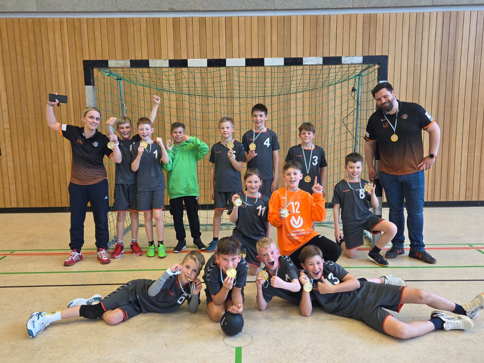 Jubelndes Jugendhandballteam der HSG Coswig mit Medaillen vor einem Handballtor, Trainer und Betreuer sind ebenfalls dabei.