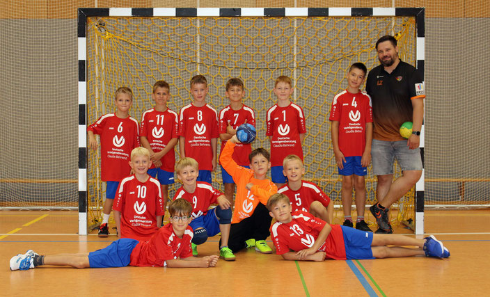 Teamfoto E-Jugend in roten Trikots mit blauer Hose vor einem Handballtor