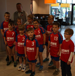 Eine Jugendhandballmannschaft der HSG Coswig mit einem erwachsenen Mann posiert für ein Gruppenfoto in Innenräumen.